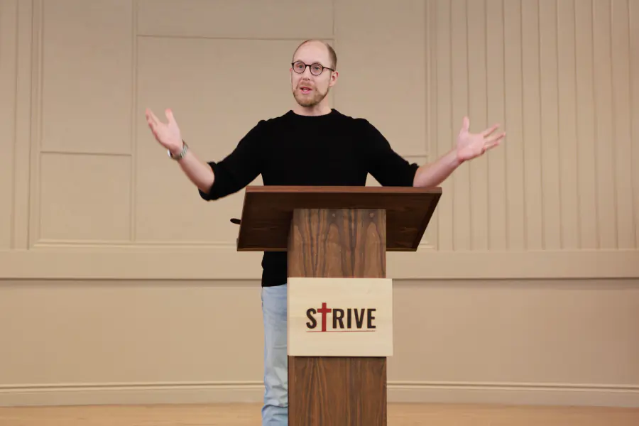 A speaker addressing the room with arms outstretched
