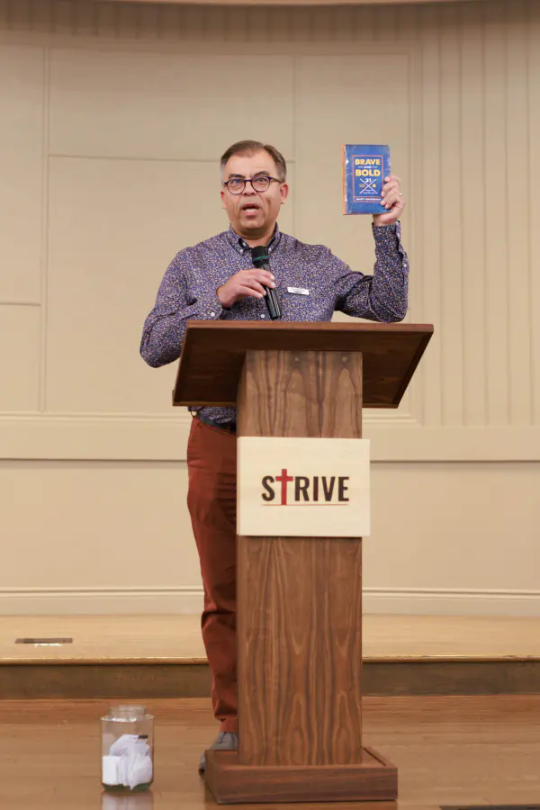 A conference speaker holding up a book from the podium